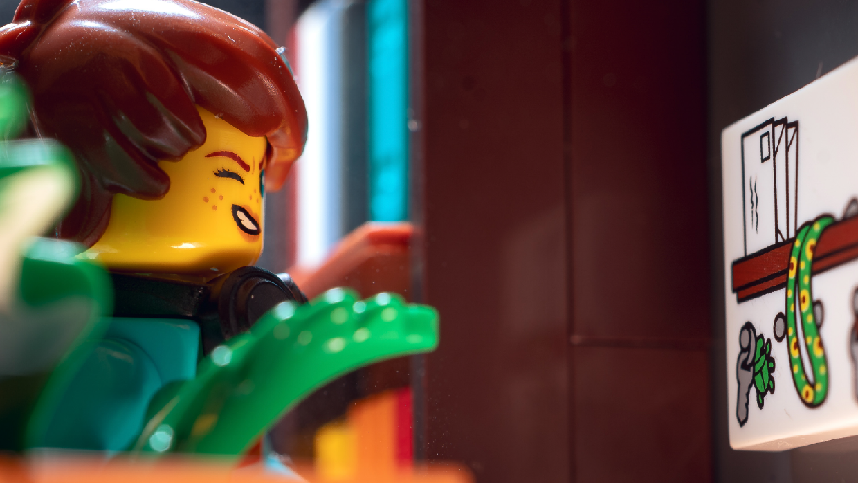 a-lego-minifigure-wearing-headphones-looks-at-a-printed-tile-depicting-a-hidden-disability-sunflower-lanyard.webp