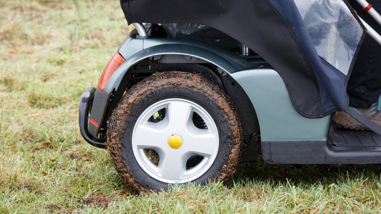 a-mud-covered-tire-on-an-all-terrain-mobility-scooter-demonstrating-its-off-road-performance-in-a-grassy-field.webp