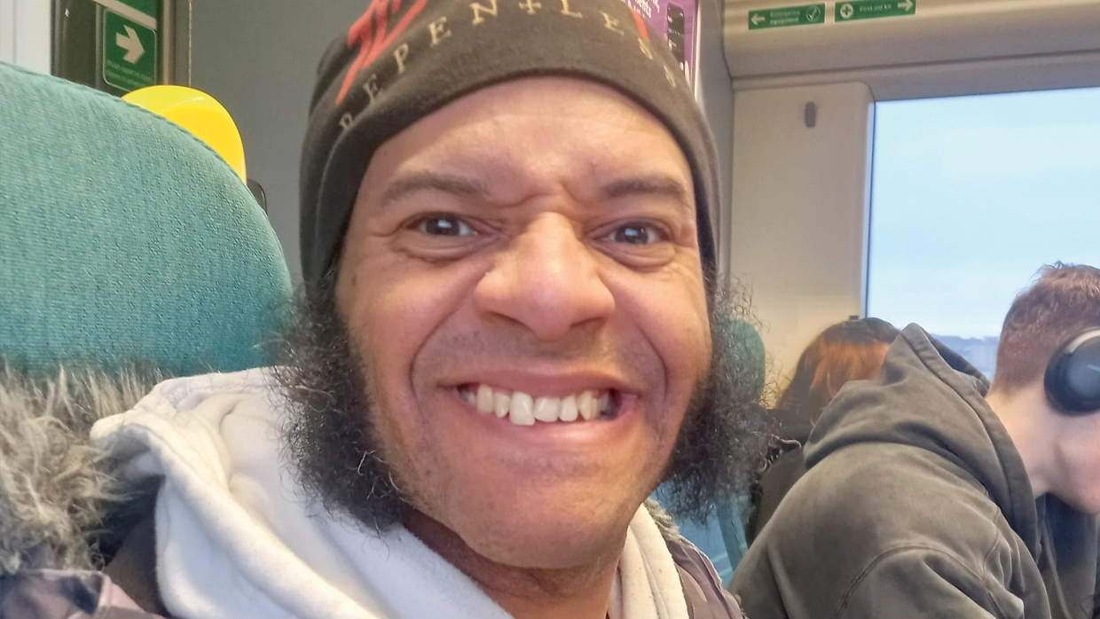a-smiling-man-in-a-beanie-and-hoodie-takes-a-selfie-while-traveling-on-a-train.webp