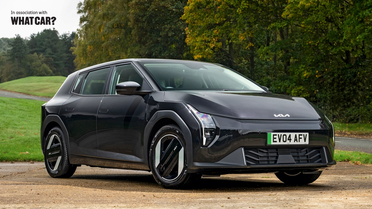 A black Kia EV4 parked on a gravel clearing amid a pleasant woodland backdrop