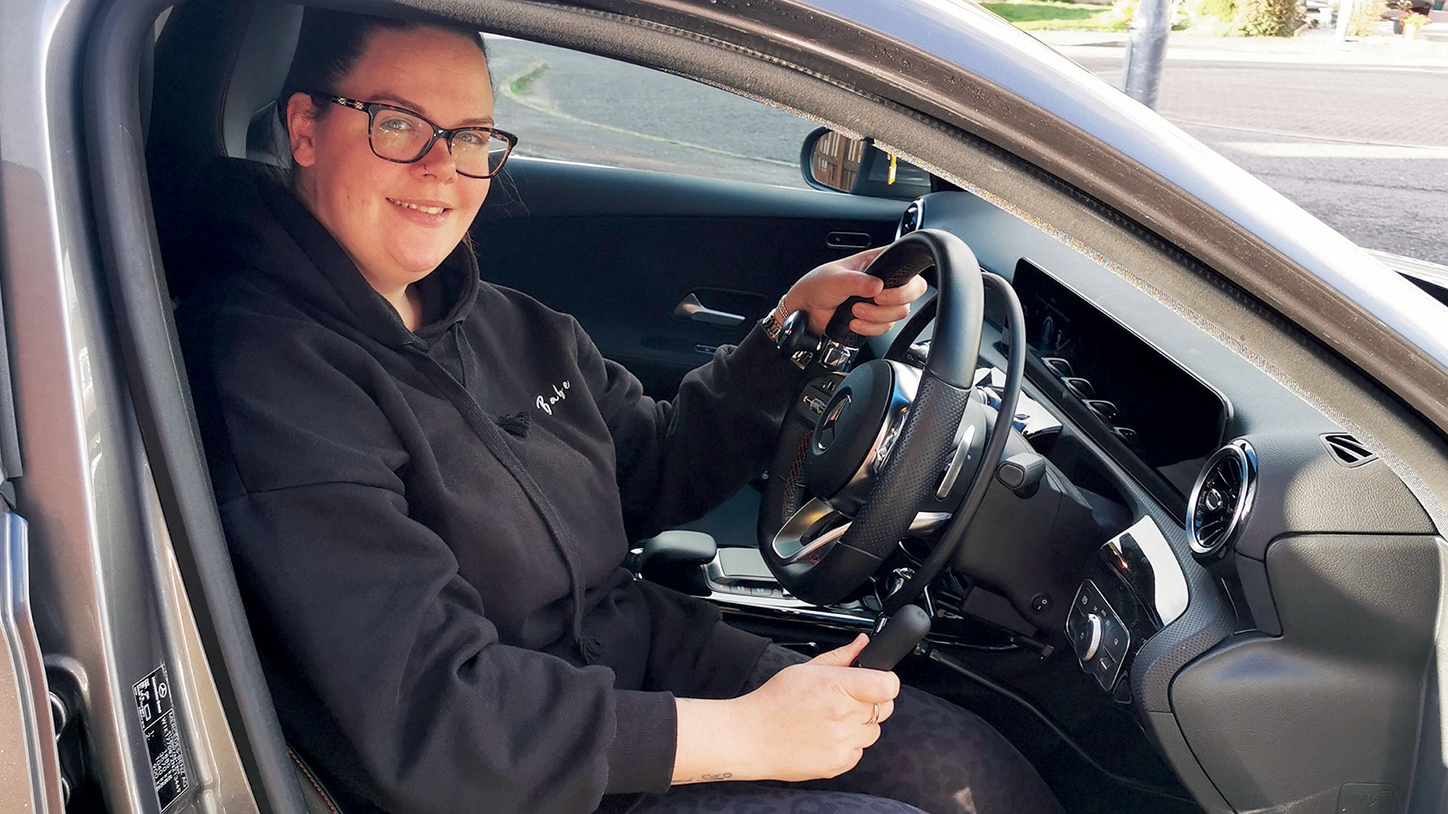 A young woman pictured in a car with hand control adaptations