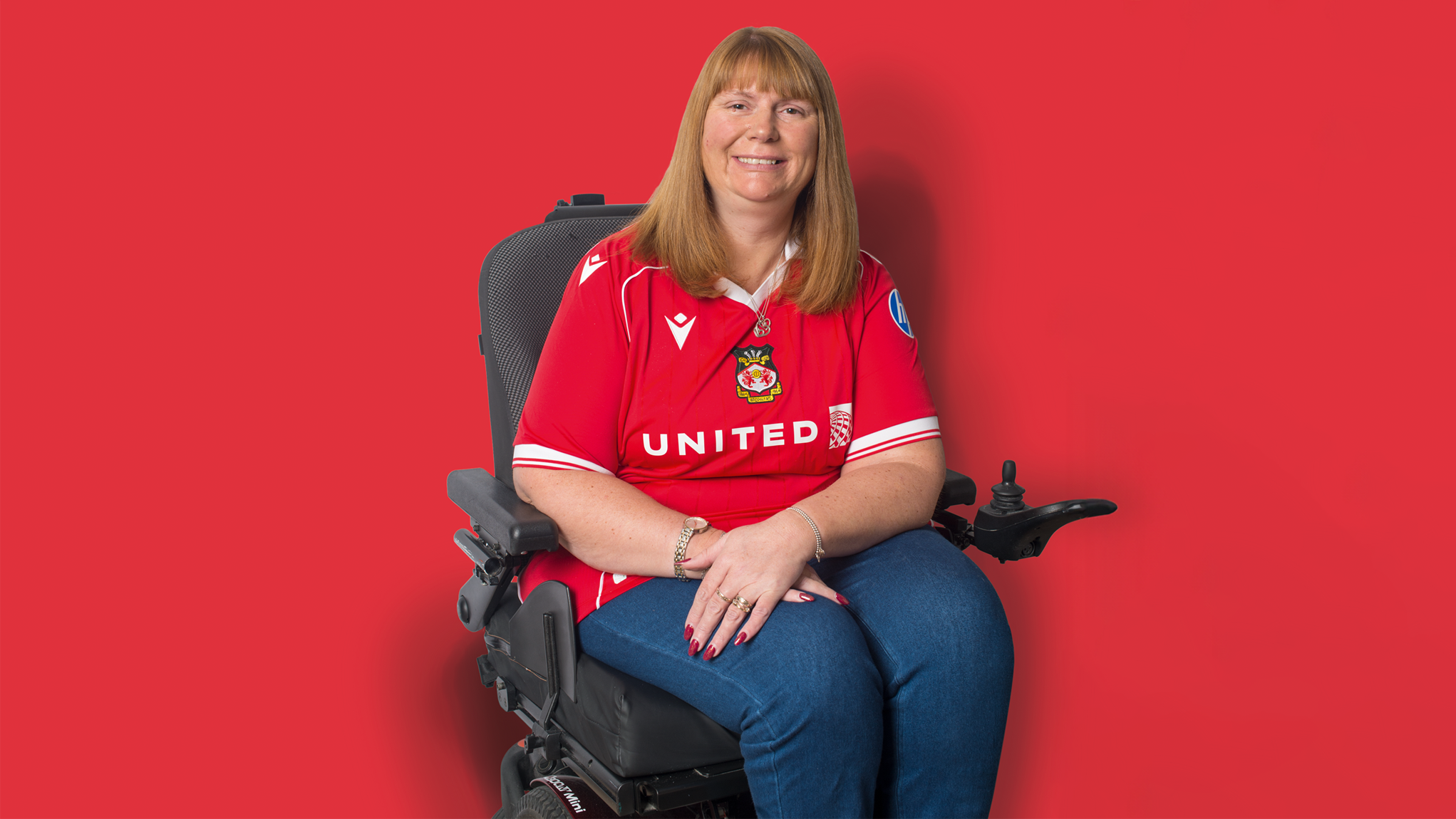 Photo of Kerry wearing her Wrexham t-shirt sitting in front of a red background