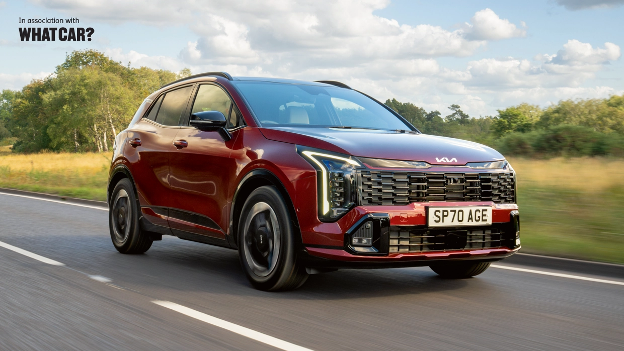 Maroon Kia Sportage driving on a rural road, with "In association with What Car?" text in the top left corner.