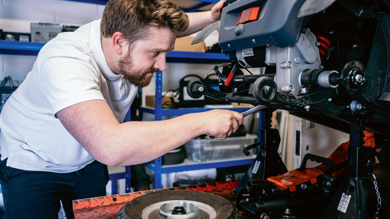 A male mechanic in a workshop carrying out a service on a mobility scooter