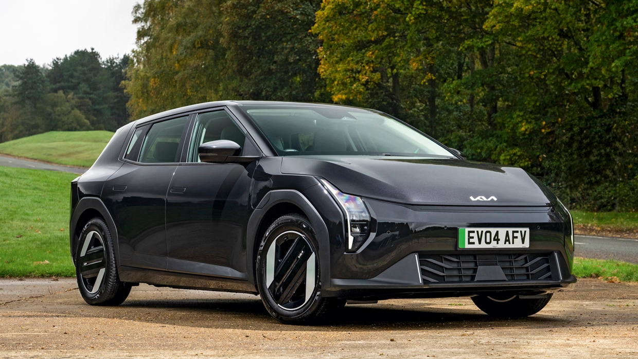 A black Kia EV4 parked on a gravel clearing amid a pleasant woodland backdrop