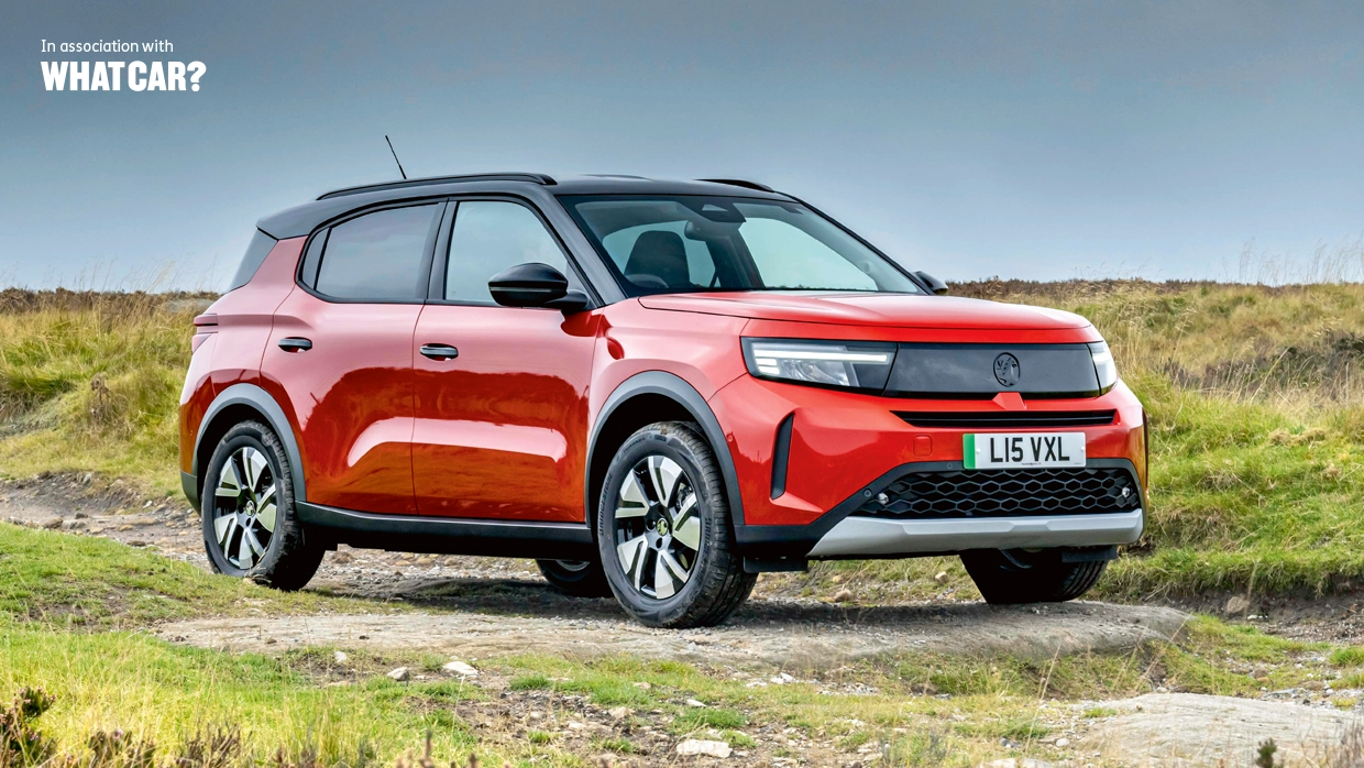 A red Vauxhall Frontera Electric SUV parked on a rural track, with "In association with What Car?" text in the top left corner.