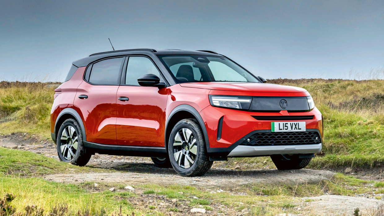 A red Vauxhall Frontera Electric SUV with a black roof parked on a rural dirt track.