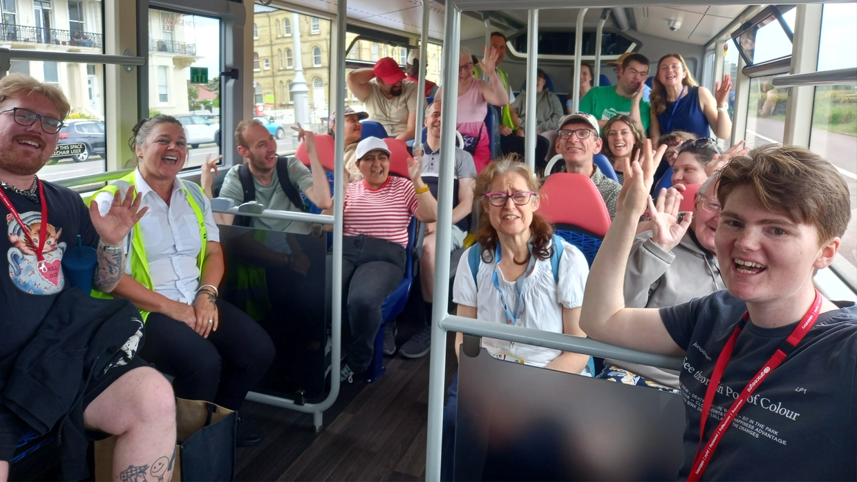 A cheerful group of people smiling and waving from their seats during a group excursion on an accessible bus.
