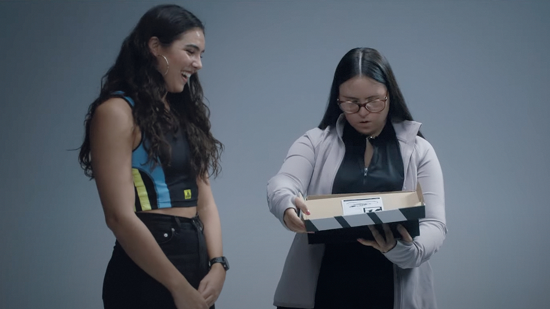Two girls side-by-side. One has Down Syndrome and is unboxing some shoes