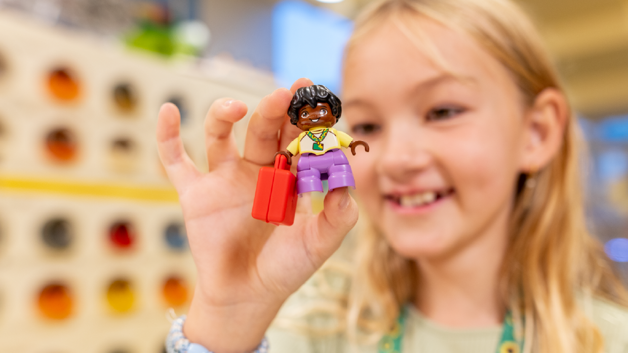 A smiling girl wearing a Hidden Disabilities Sunflower lanyard holds up a custom LEGO minifigure with a matching lanyard