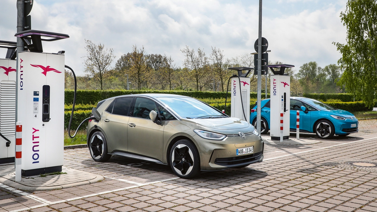 A metallic gold Volkswagen ID.3 electric car charging at an IONITY ultra-fast charging station next to a light blue Volkswagen ID.3 charging at an IONITY fast charger in the background.