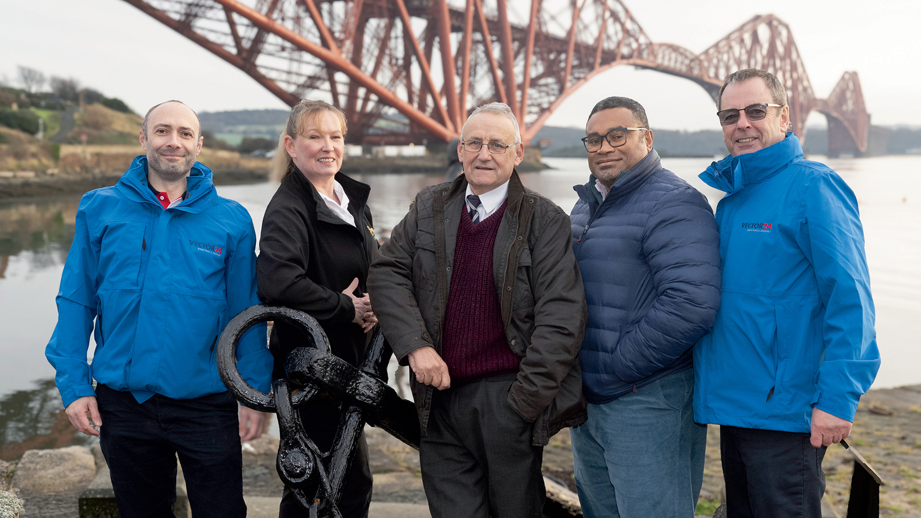 Leon Fisher (left) and for other people stood smiling at the camera in front of a bridge 