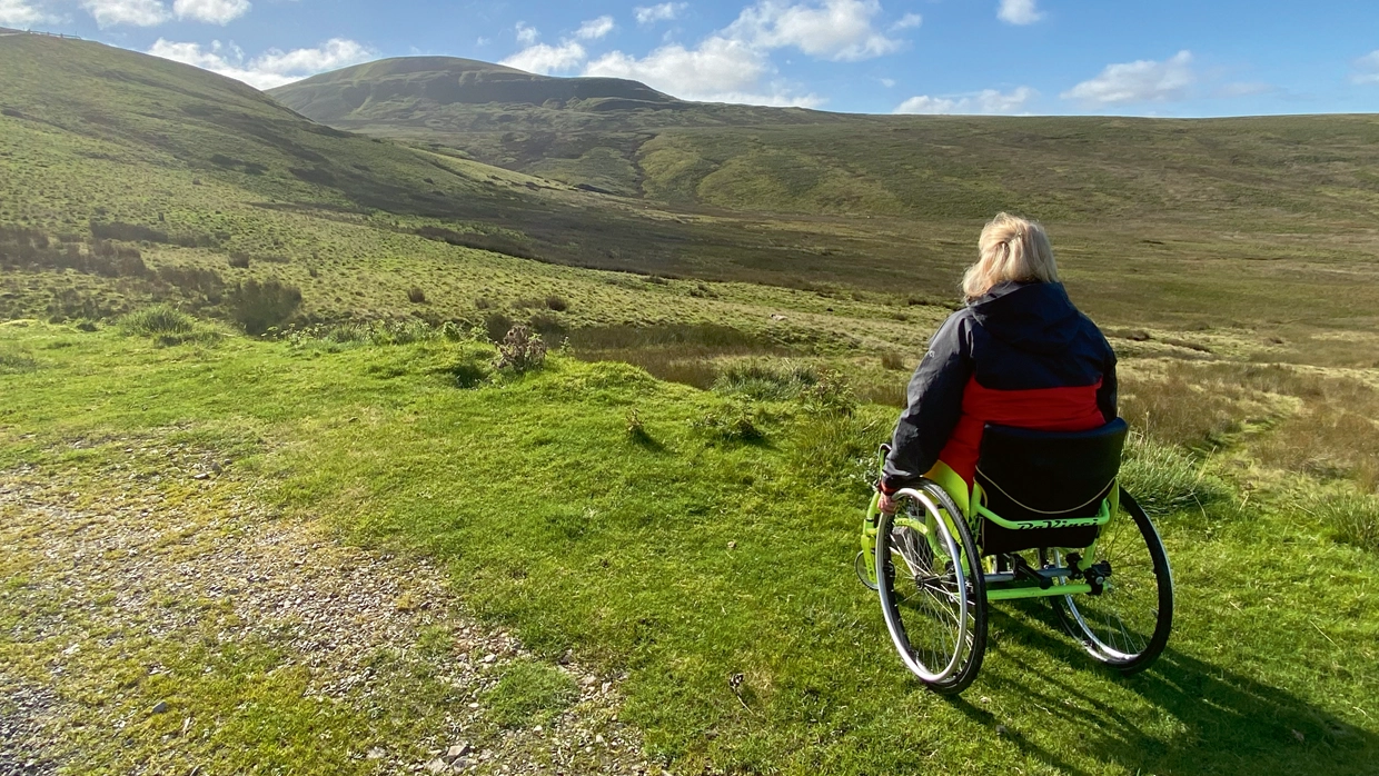 Debbie in her wheelchair out in the countryside.webp