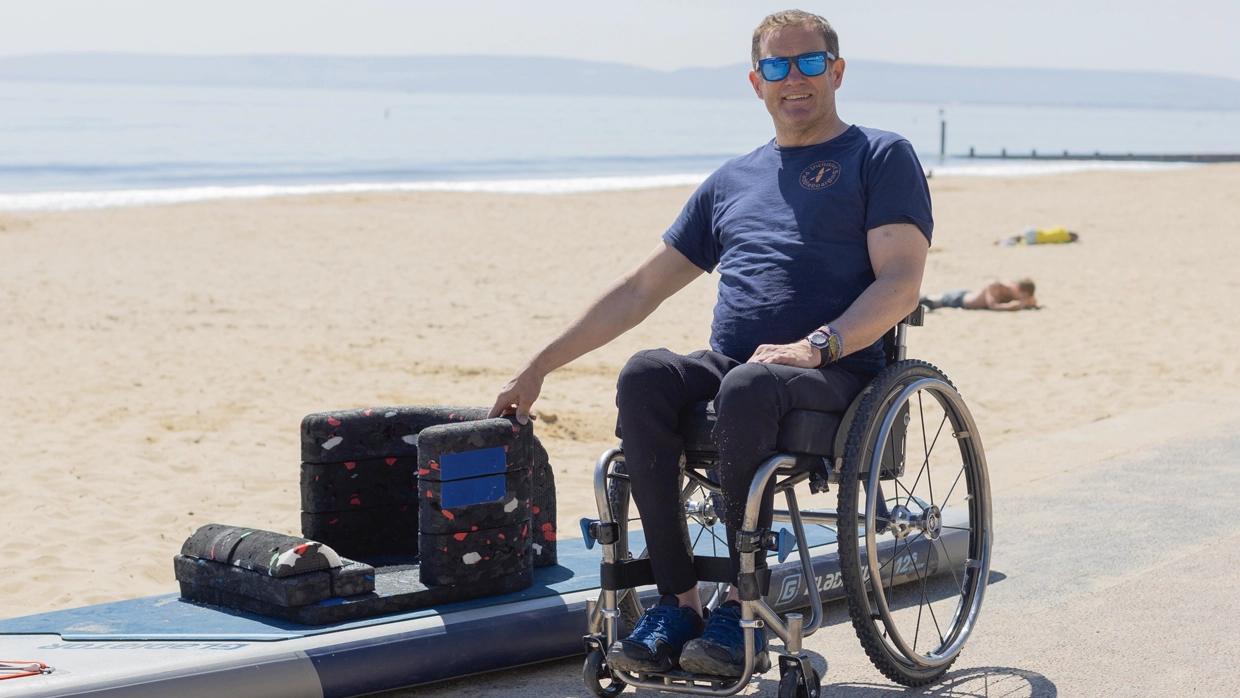 Will by his paddle board in his wheelchair by the beach.webp